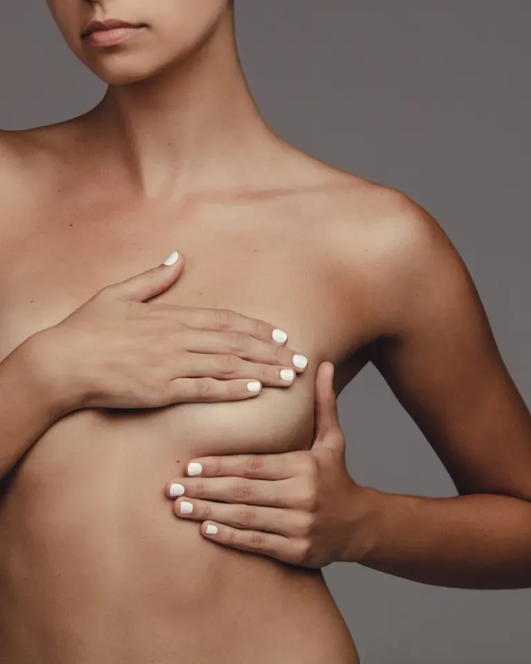 Hands covering a bare chest against a gray background