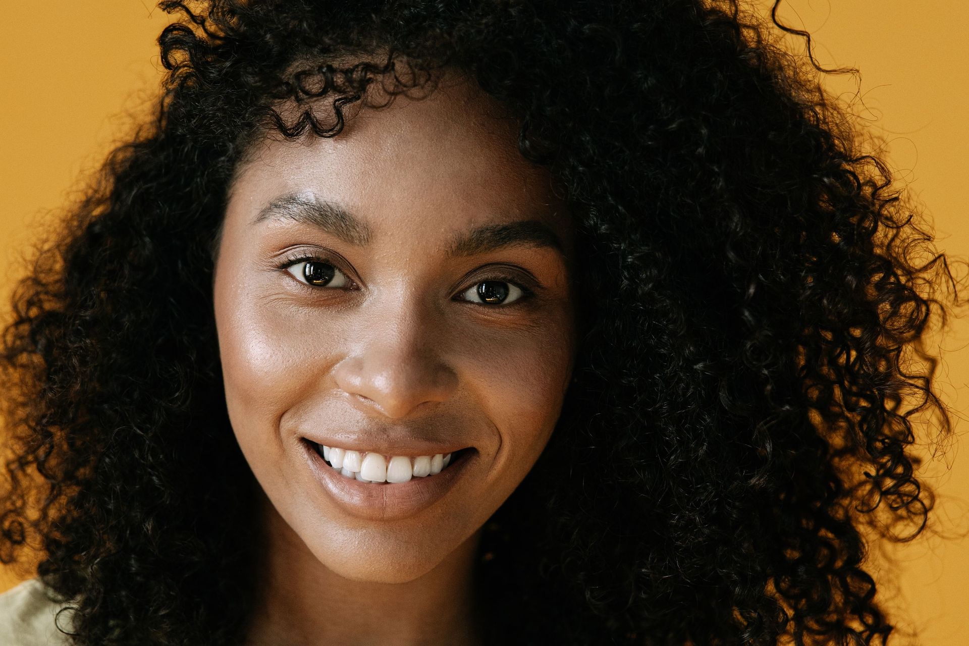 Smiling person with curly dark hair against a warm yellow background