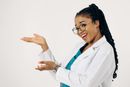 Smiling doctor in white coat and glasses gesturing with open hands against a plain background