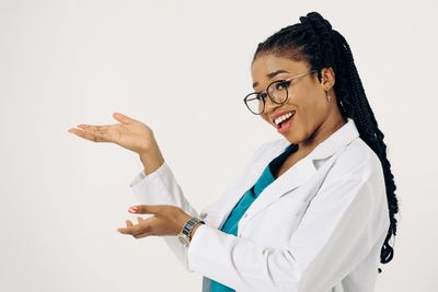 Smiling doctor in white coat and glasses gesturing with open hands on a plain background
