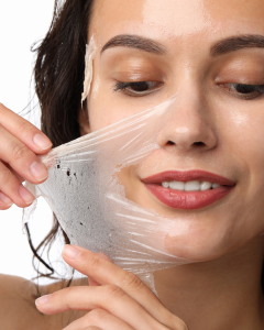 Woman peeling off a translucent facial mask, revealing smooth skin and a slight smile