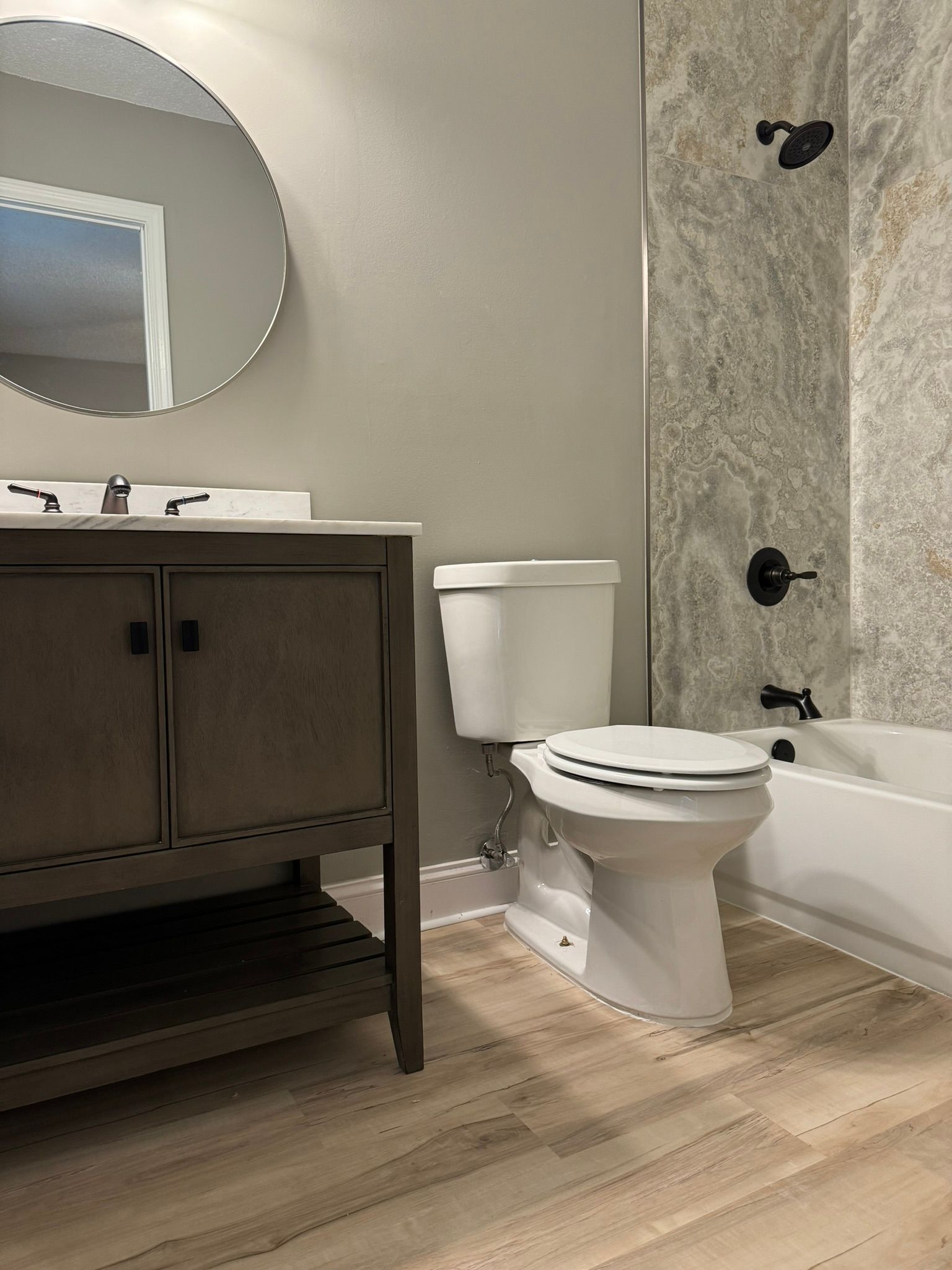 Bathroom with vanity, toilet, and tub/shower combo. Grey walls, neutral wood-look floor.
