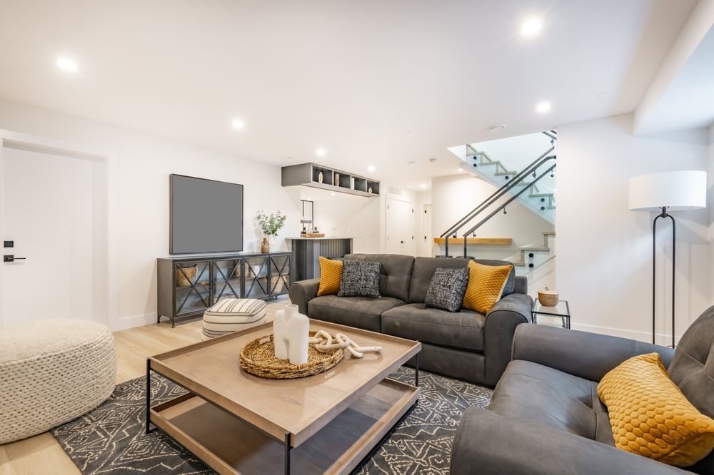 Modern basement living room with grey sofa, coffee table, and stairs.