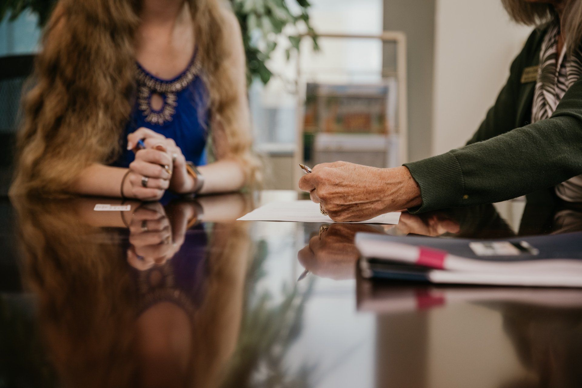 Two people in a meeting, hands over papers on a reflective conference table