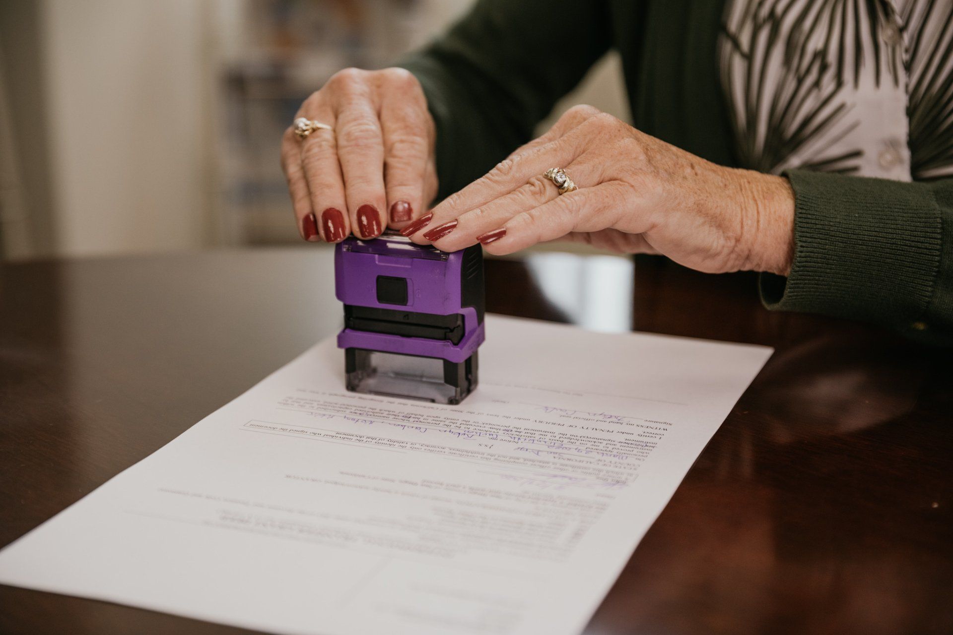 Person stamping a document with a purple stamp; hands and paper in focus on a wooden table.
