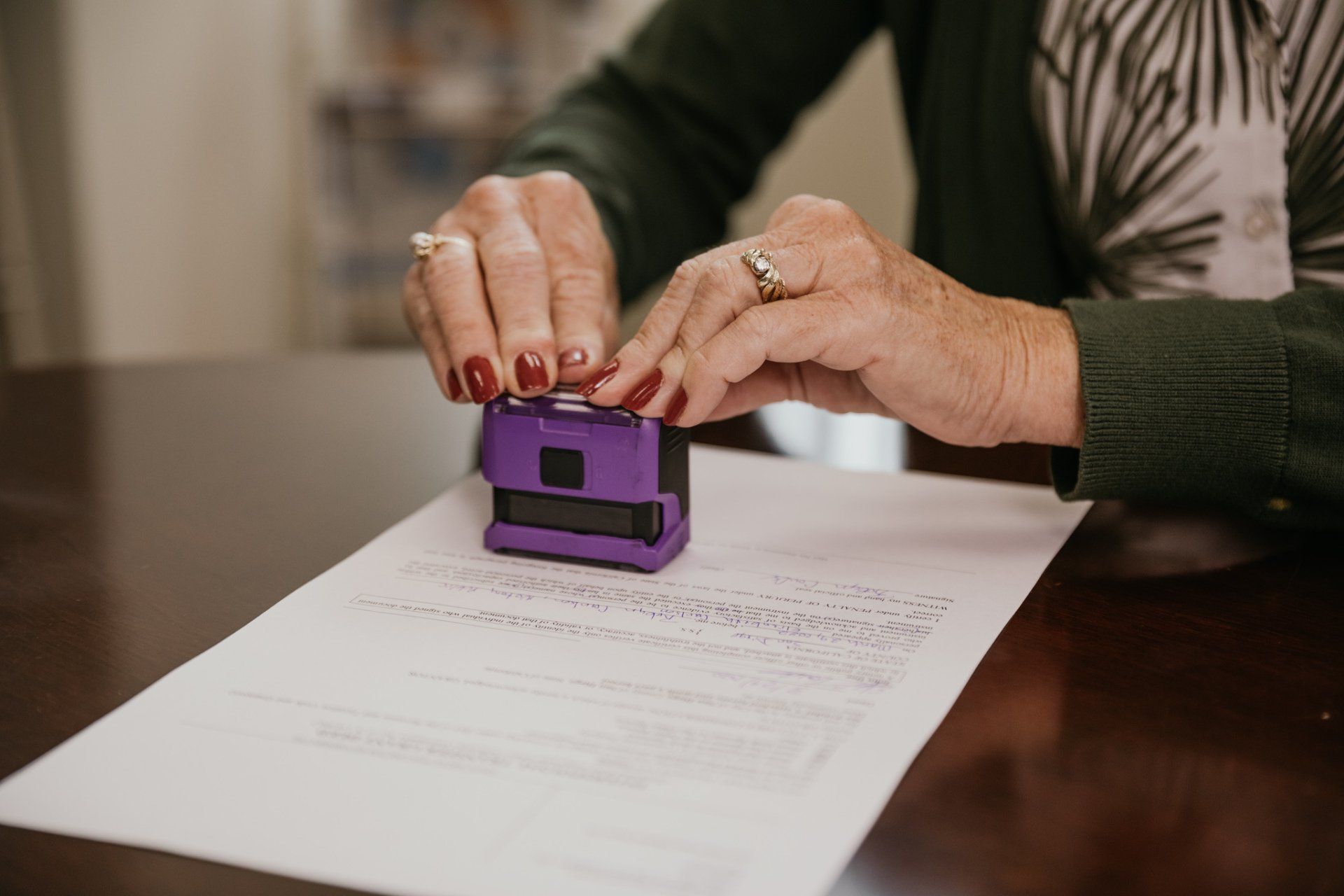 Hands stamping a purple notary seal onto a document on a desk