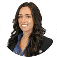 A woman with long dark hair is smiling and wearing a blue shirt and a black jacket.