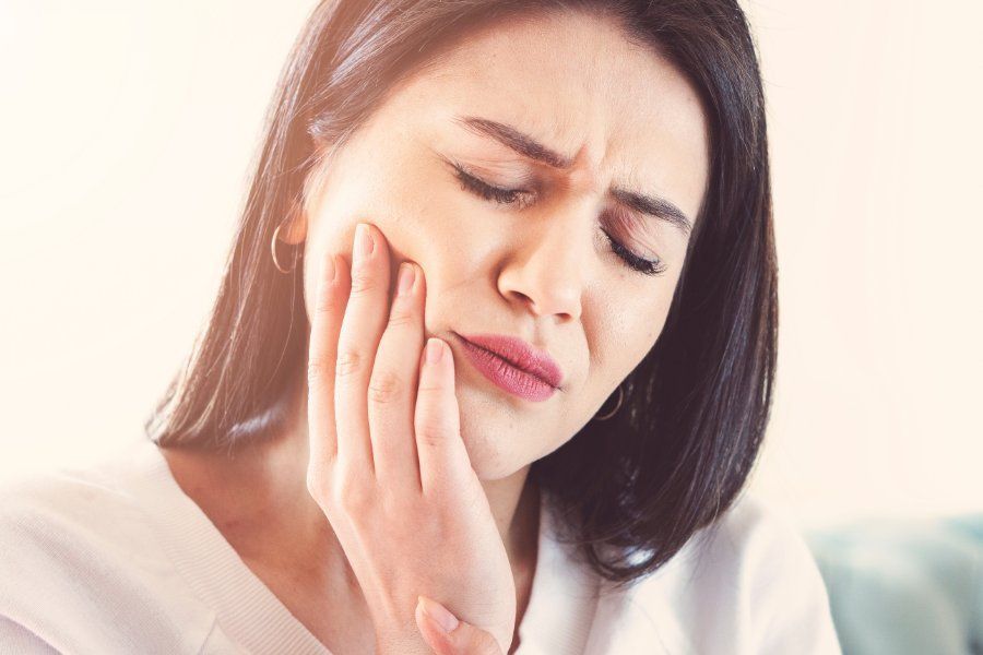 Woman with a pained expression, hand on cheek, likely experiencing a toothache.