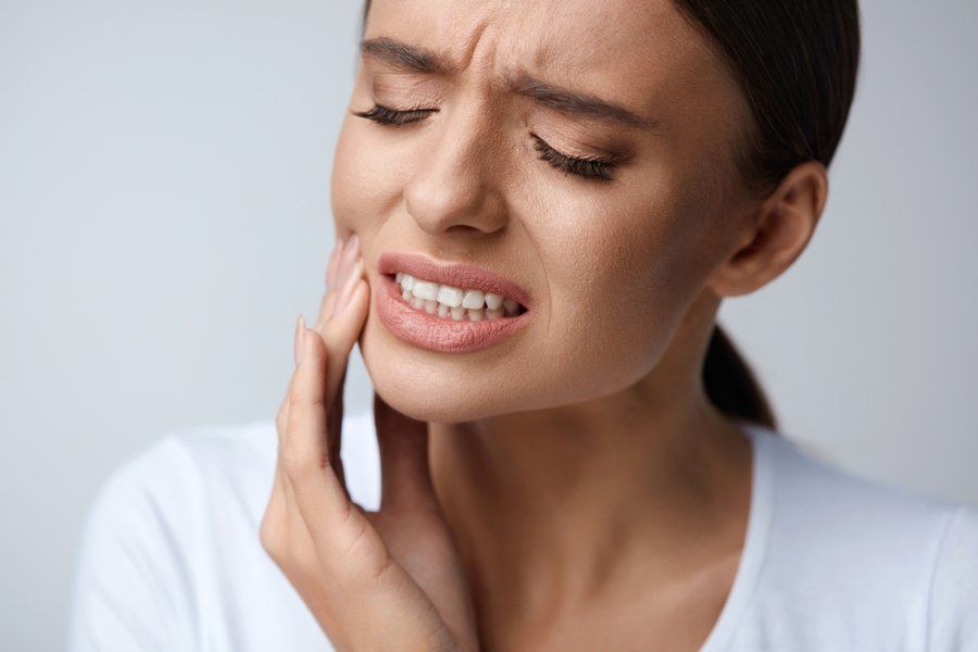 Woman with closed eyes and grimace holding her cheek in pain.