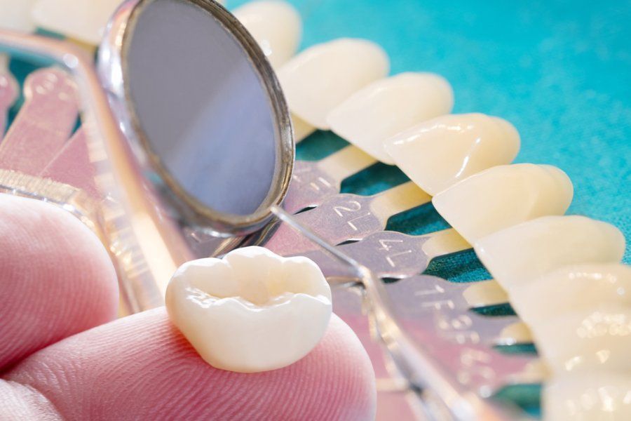 Hand holding dental crown, with mirror and shade guide in background.