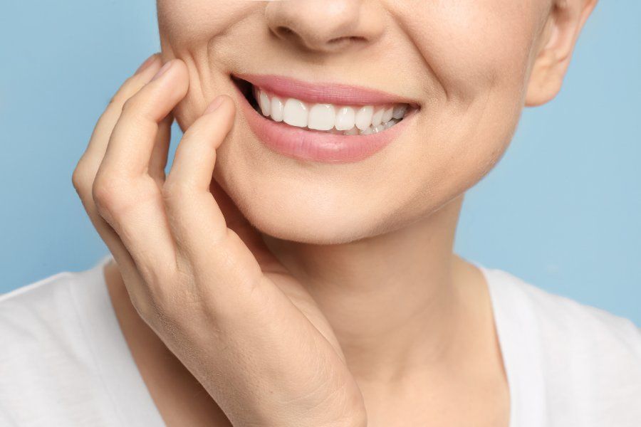 Woman smiling, touching cheek with hand, showing white teeth, against blue background.
