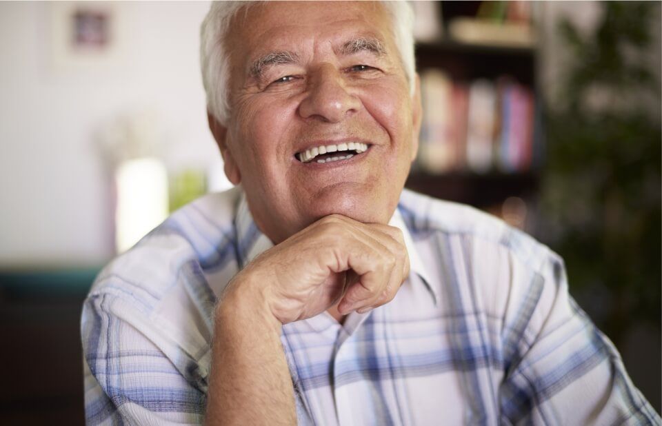 Smiling senior citizen resting chin on hand, wearing a blue and white plaid shirt.