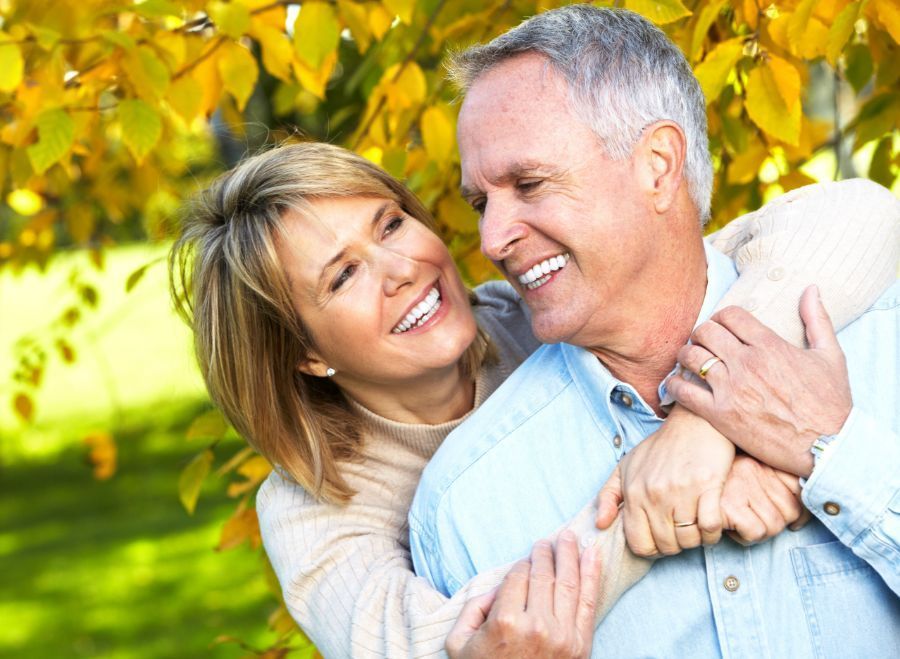 Smiling couple embracing outdoors, surrounded by yellow fall foliage.
