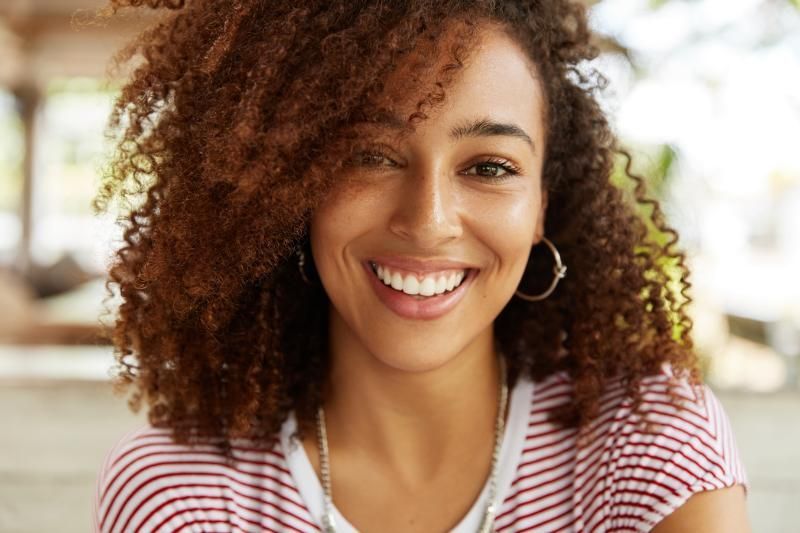 Woman with curly brown hair smiles brightly, wearing a striped shirt and hoop earrings.