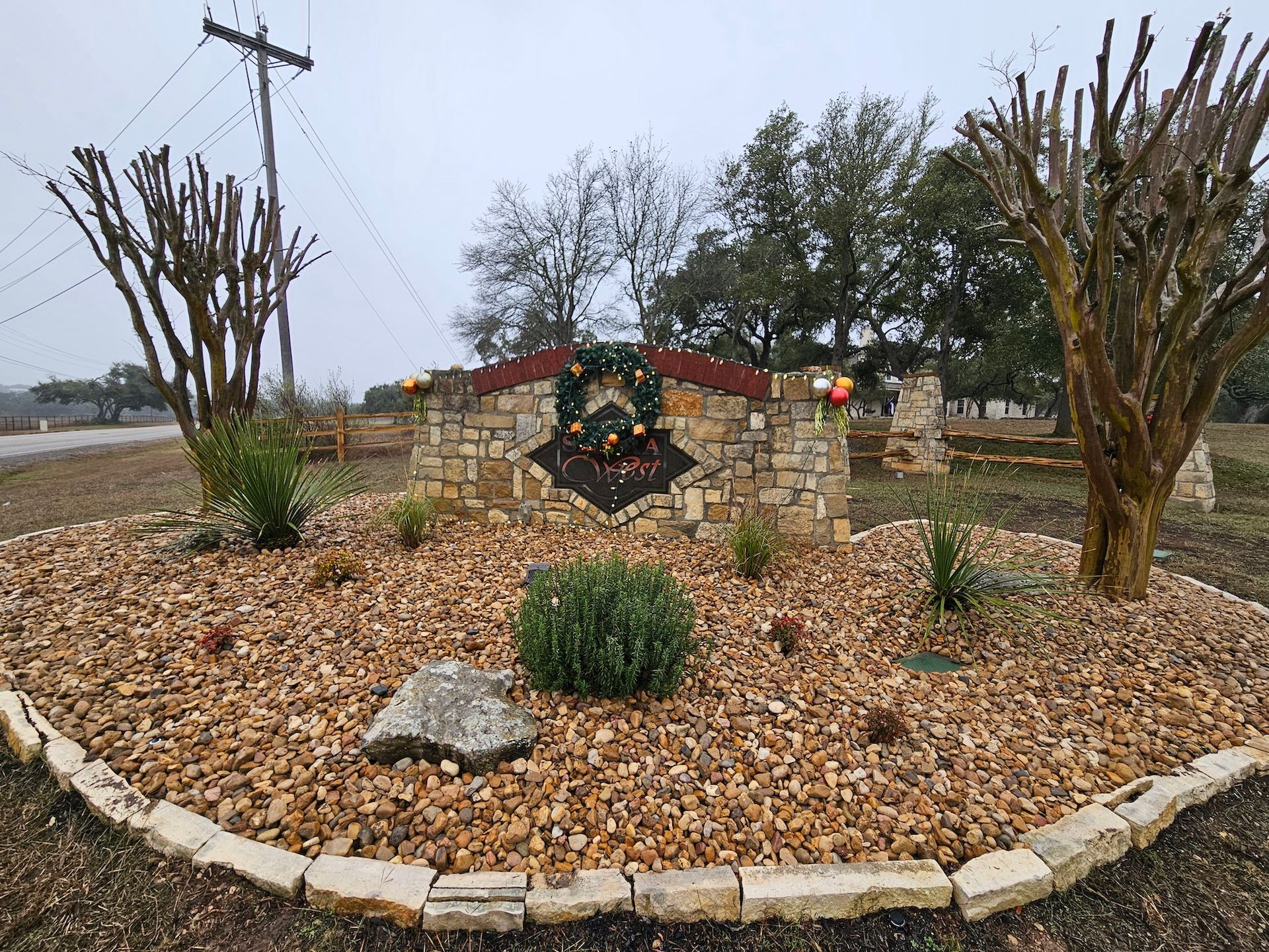 A stone sign with a wreath on it is surrounded by gravel and trees.