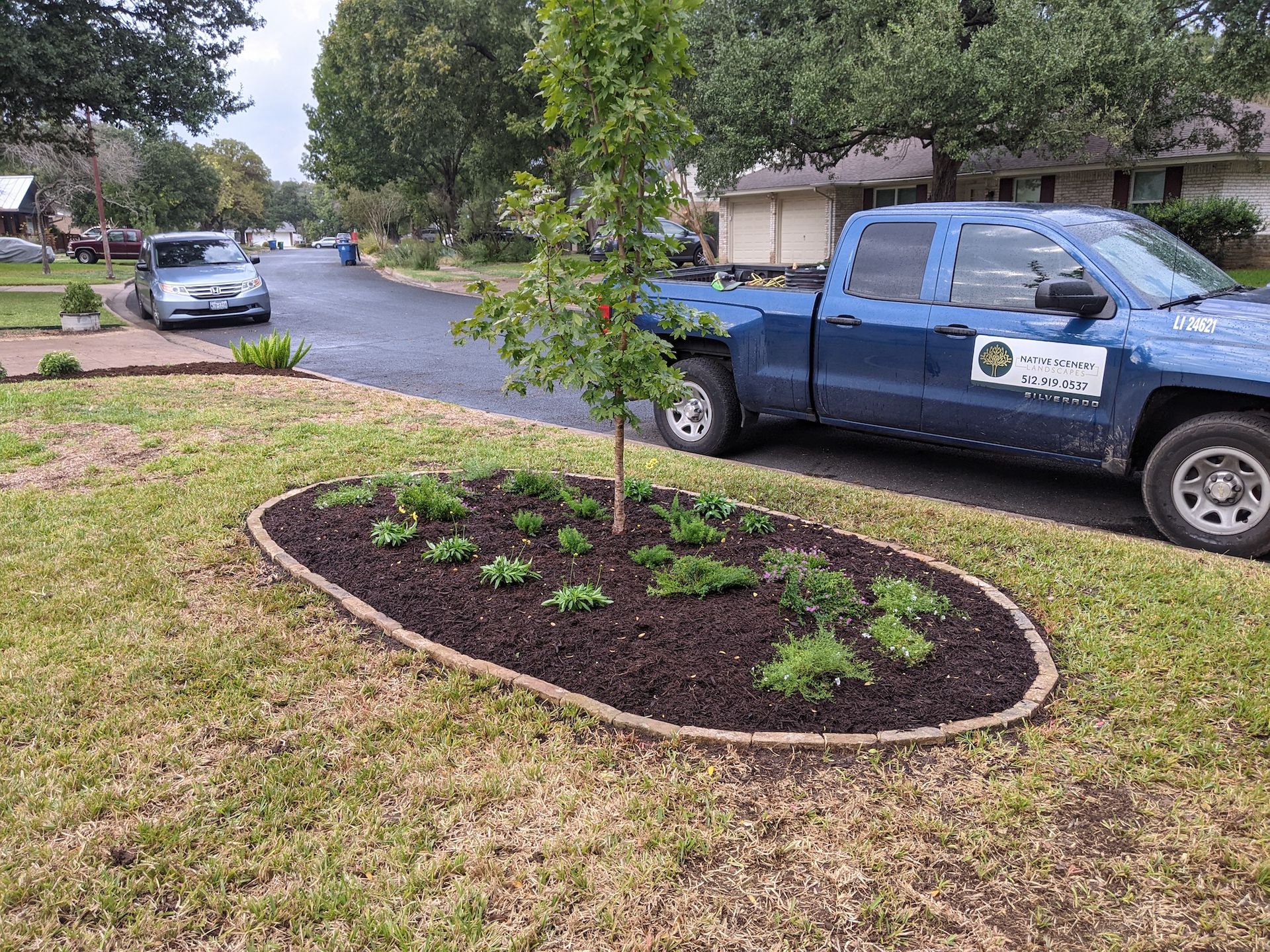 A blue truck is parked next to a tree in a yard.