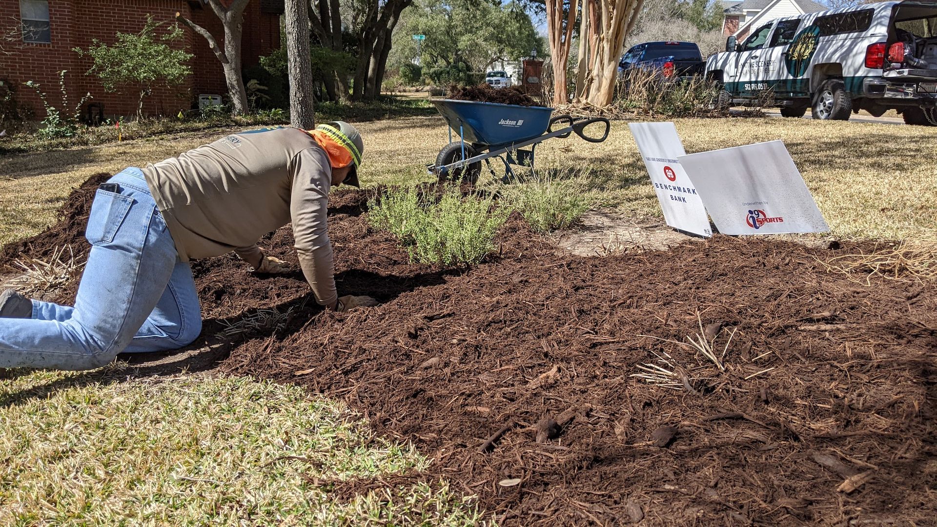 A man is kneeling down in a pile of mulch in a yard.