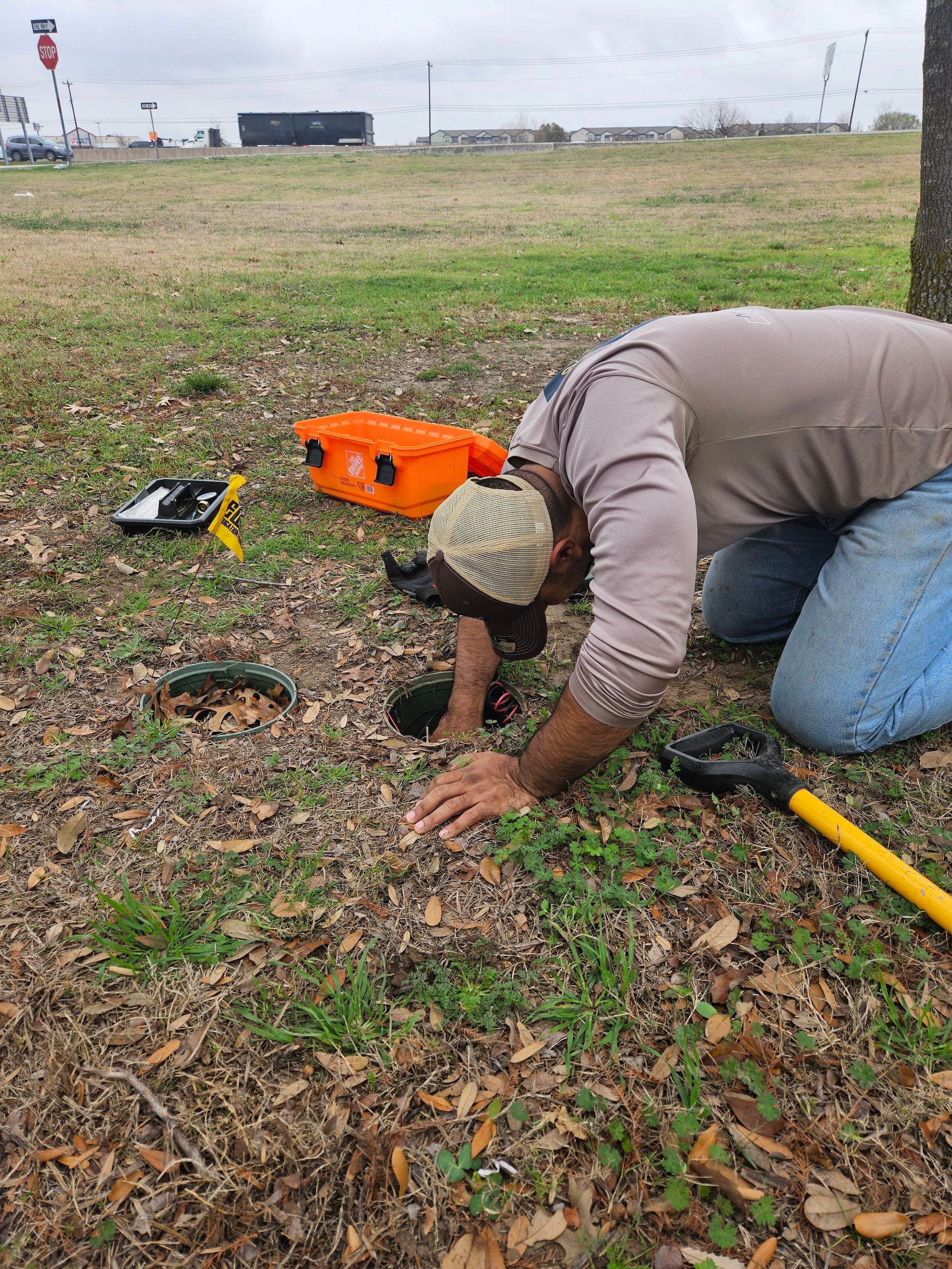 A man is kneeling down in the grass looking at a hole in the ground.