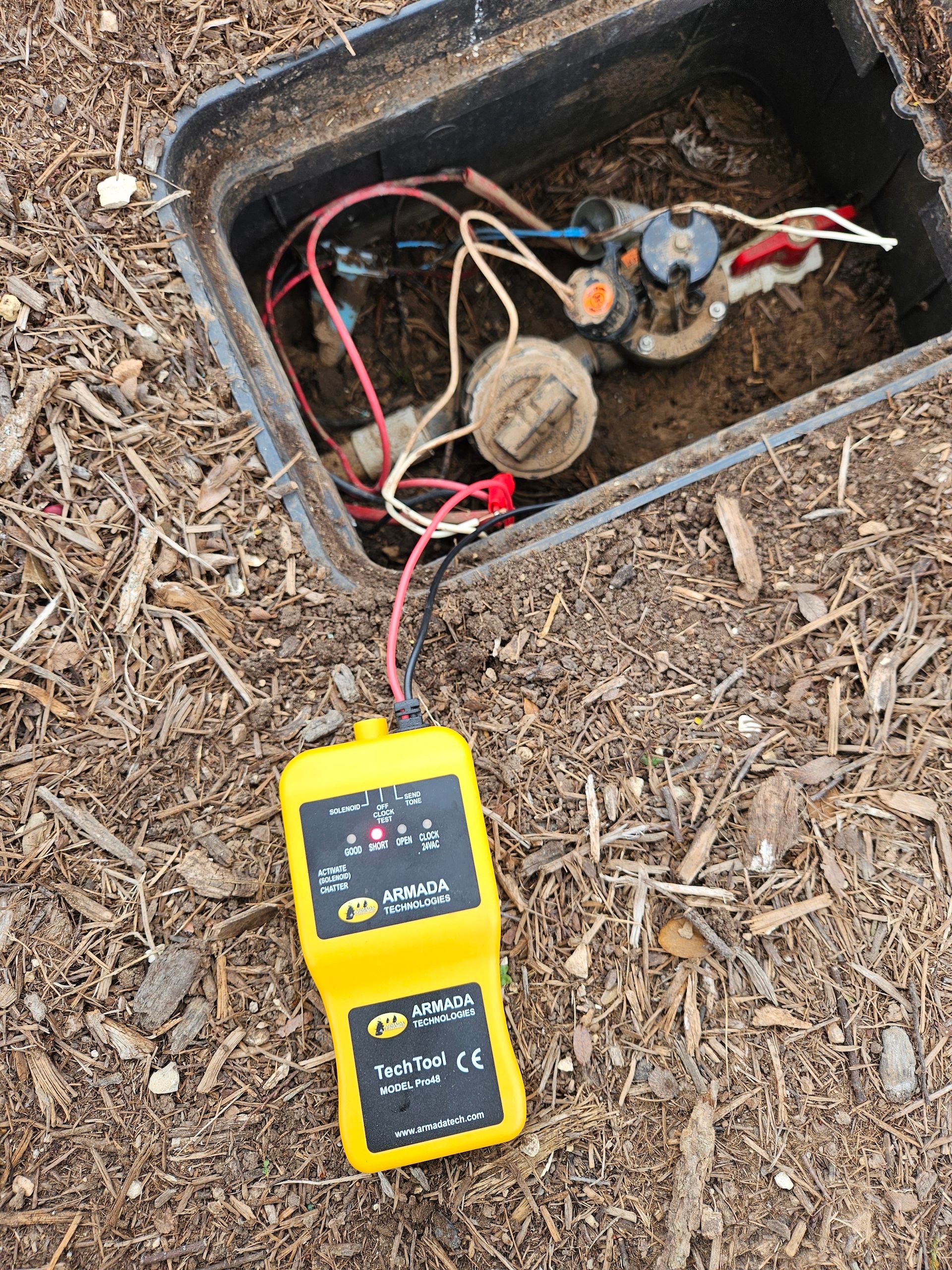 A yellow device is sitting in the dirt next to a water meter.