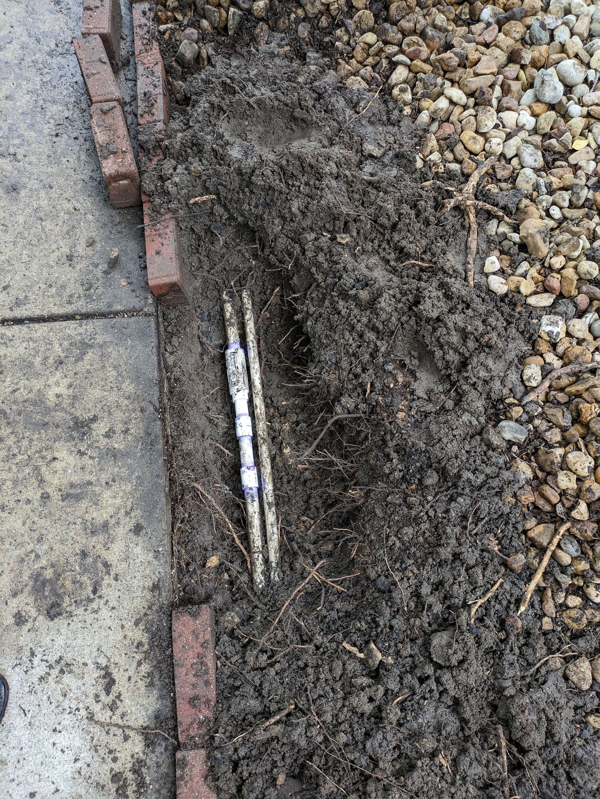 A piece of metal is sticking out of the ground next to a brick wall.