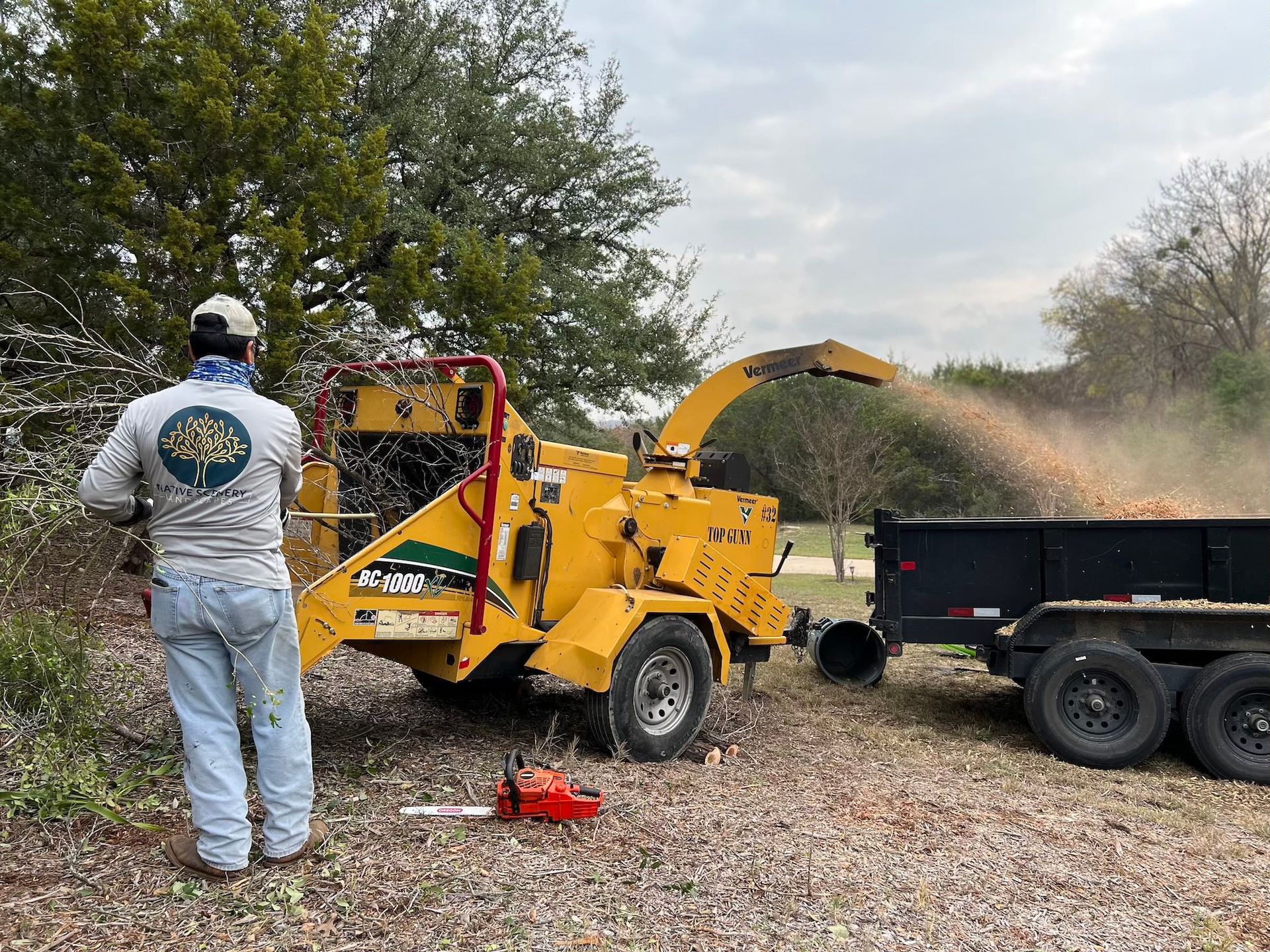 A man is standing in front of a tree chipper.
