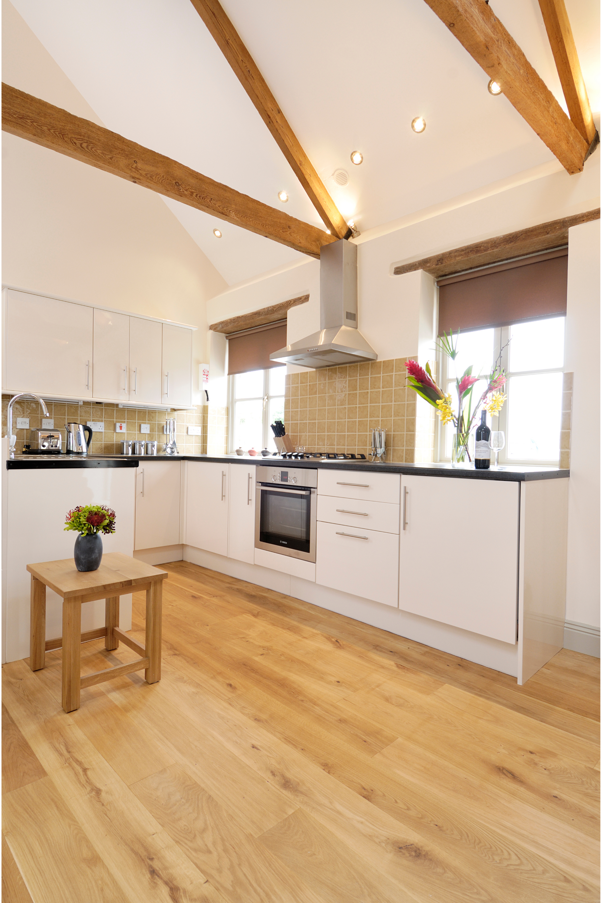 Modern kitchen with light wood floors, white cabinets, and exposed wooden beams.