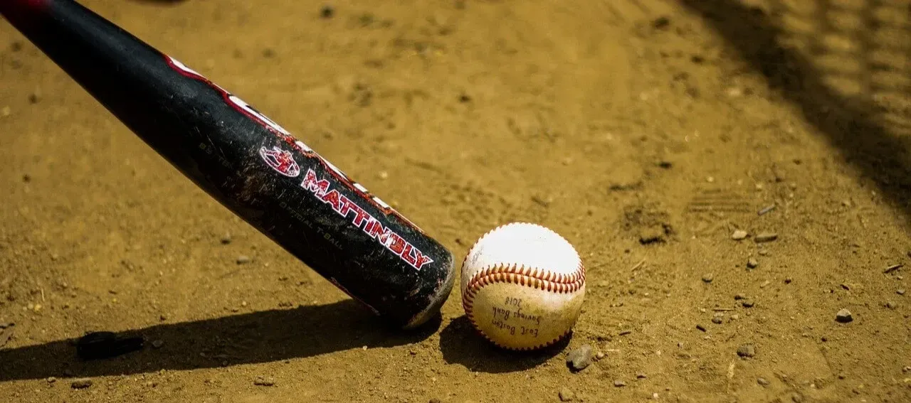 A black baseball bat rests on a dirt field next to a scuffed white baseball.