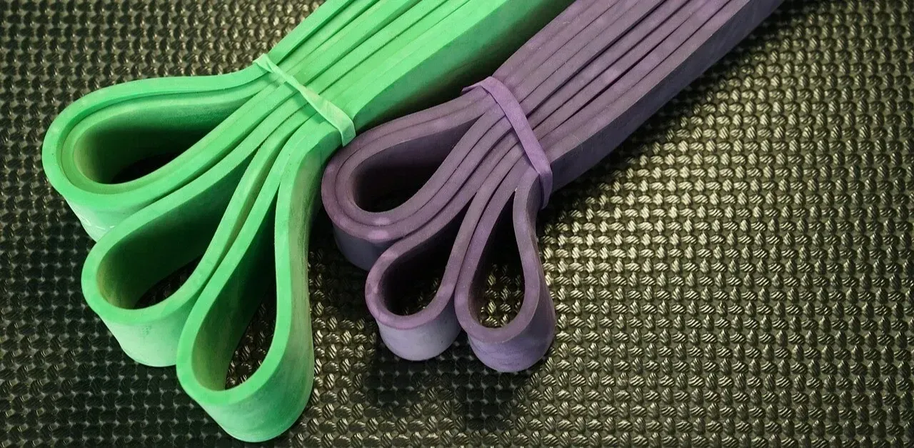 Two looped resistance bands, one green and one purple, rest on a textured black surface.
