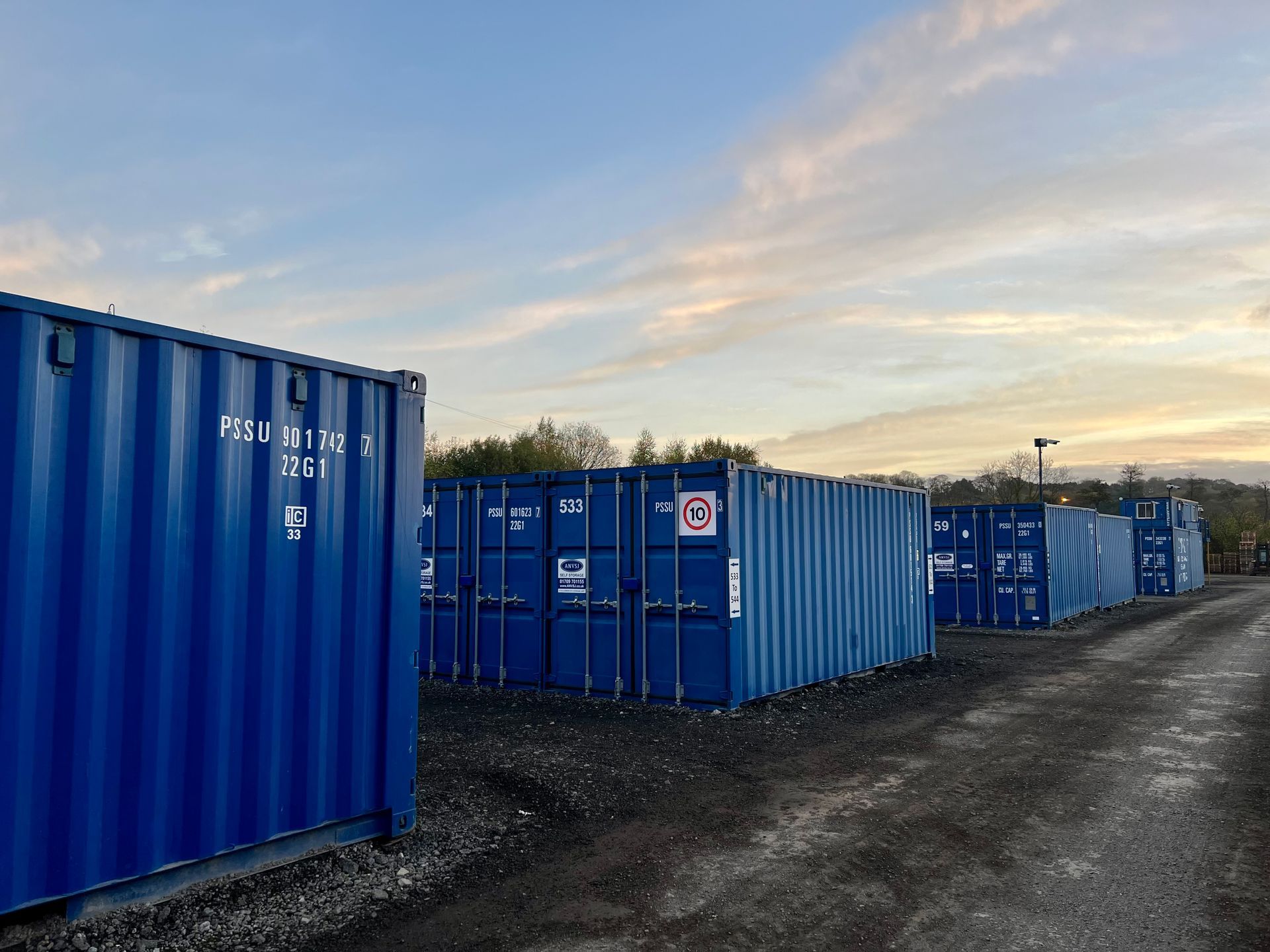 A row of blue shipping containers are lined up on road ANVSJ
