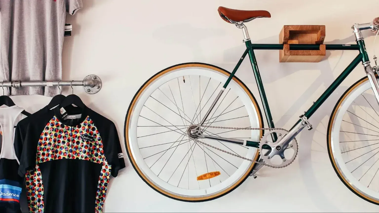 A green bicycle hangs on a wall above cycling jerseys displayed on a metal rack.