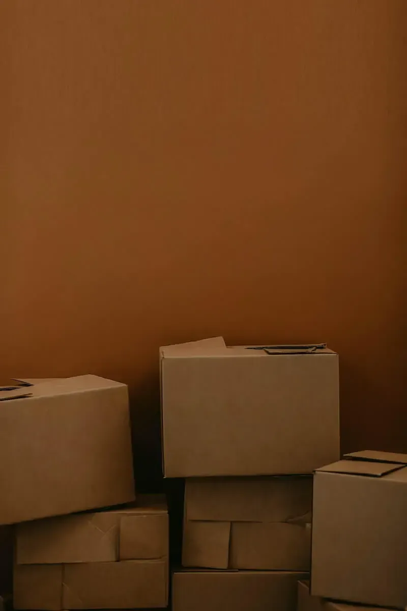 A stack of plain brown cardboard boxes sitting against a solid, dark orange wall.