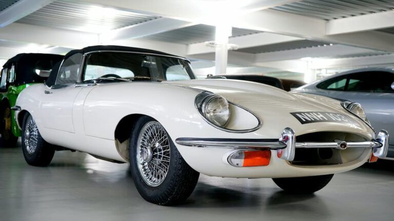 A vintage white Jaguar E-Type convertible parked inside a showroom with wire-spoke wheels.