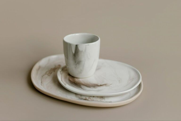 A marble-patterned ceramic cup rests on a small matching plate, both placed atop a larger oval platter in a neutral room.