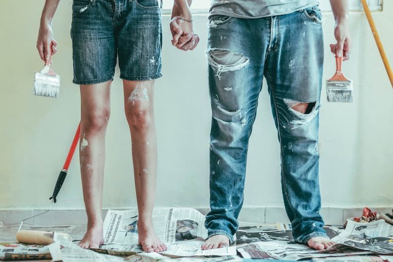 Two people, holding hands and barefoot on newspaper, are standing in a room