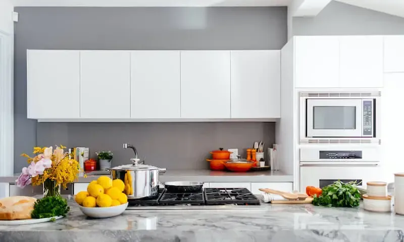 A modern kitchen featuring white cabinets, a grey backsplash, stainless steel appliances, and a marble countertop.