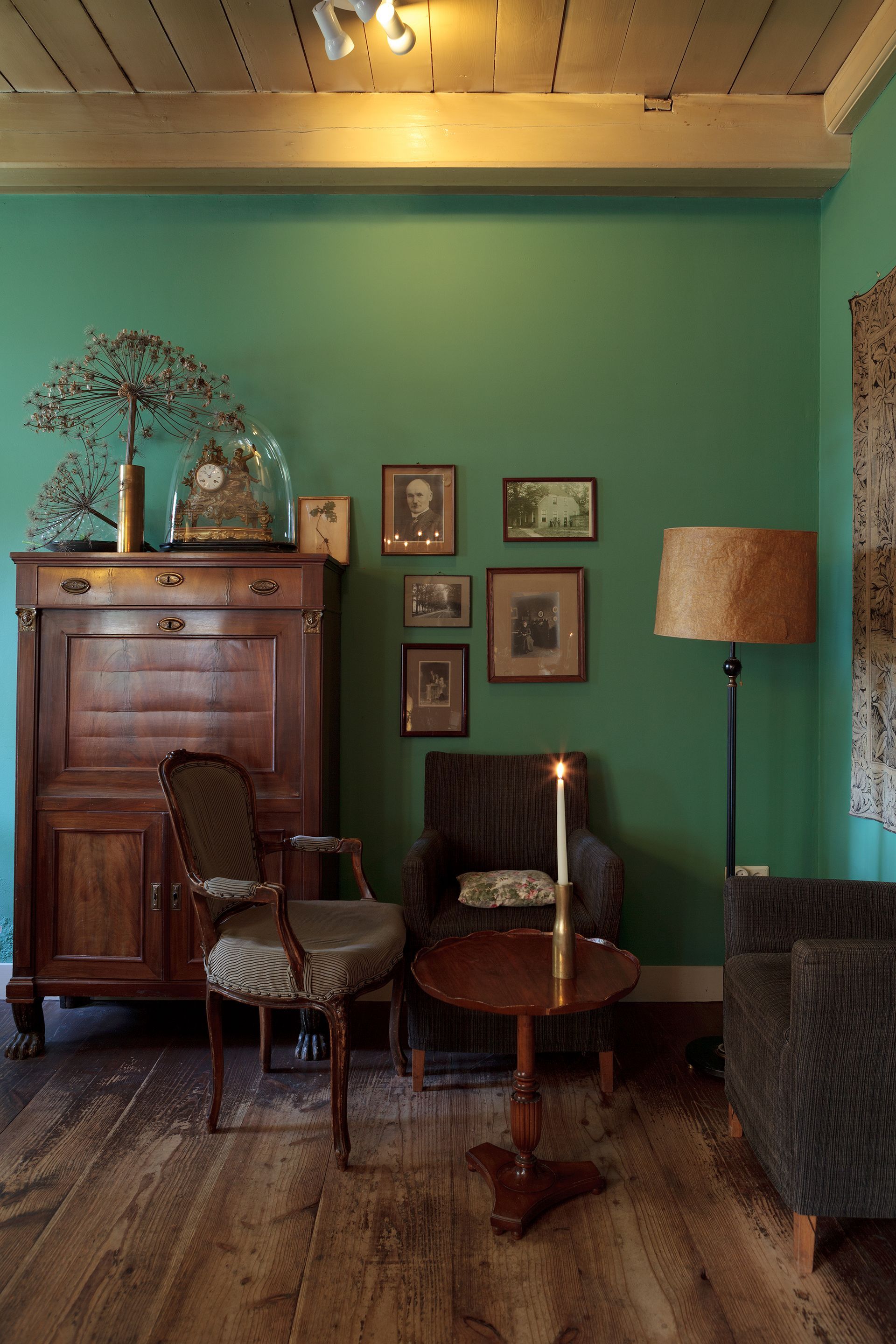 Gezellige kamer met blauwgroene muren, antieke meubels, een fotogalerij en een staande lamp in warme tinten.