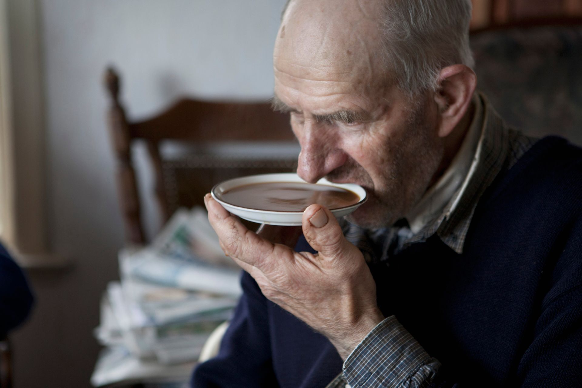 Een oudere man drinkt koffie uit zijn schotel