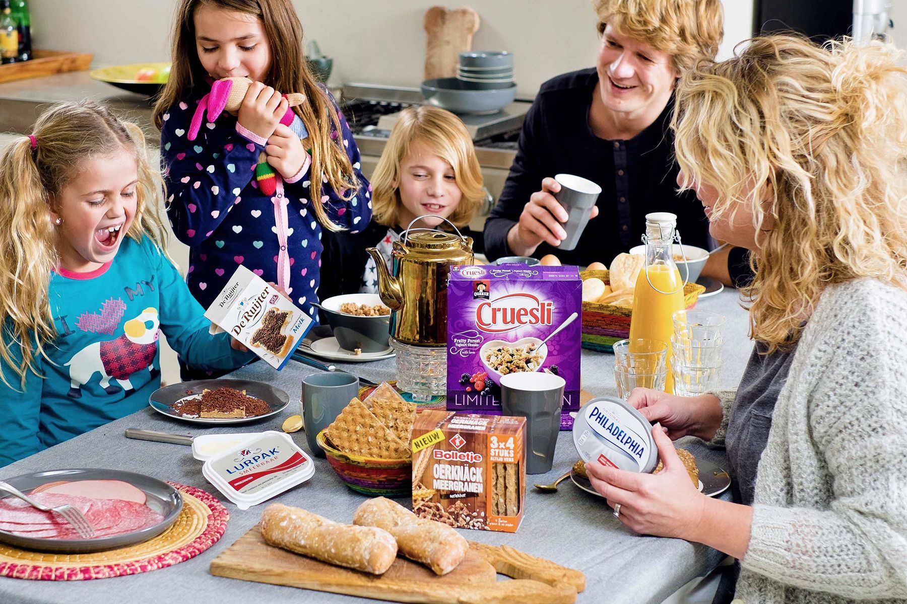 Gezin aan tafel genietend van ontbijt, inclusief ontbijtgranen, brood en vruchtensap. keukensetting. Voor Albert Heijn