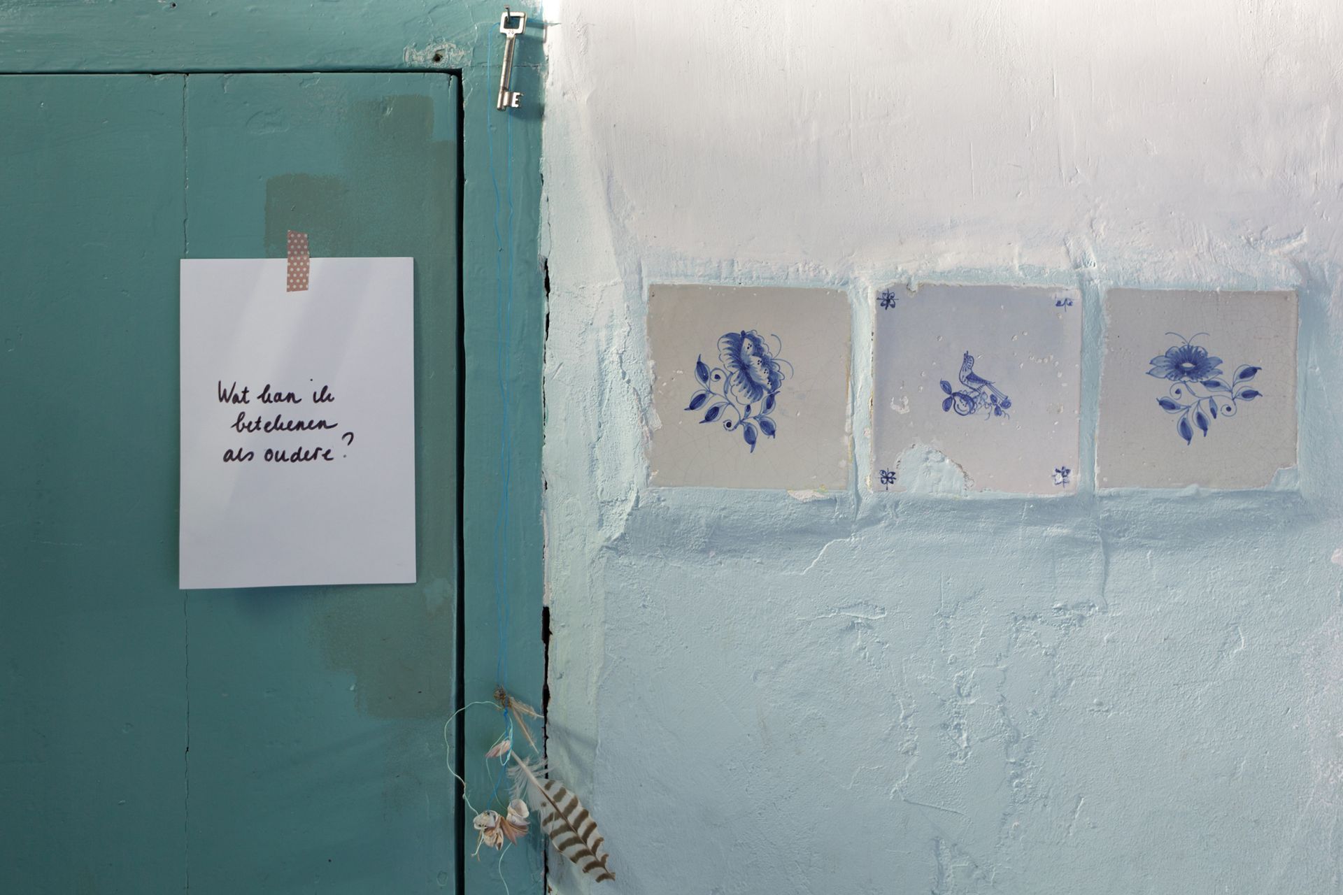 Turquoise deur met een briefje erop geplakt, naast een blauwe muur met drie Delfts blauwe tegeltjes.Foto Elise Klinkert