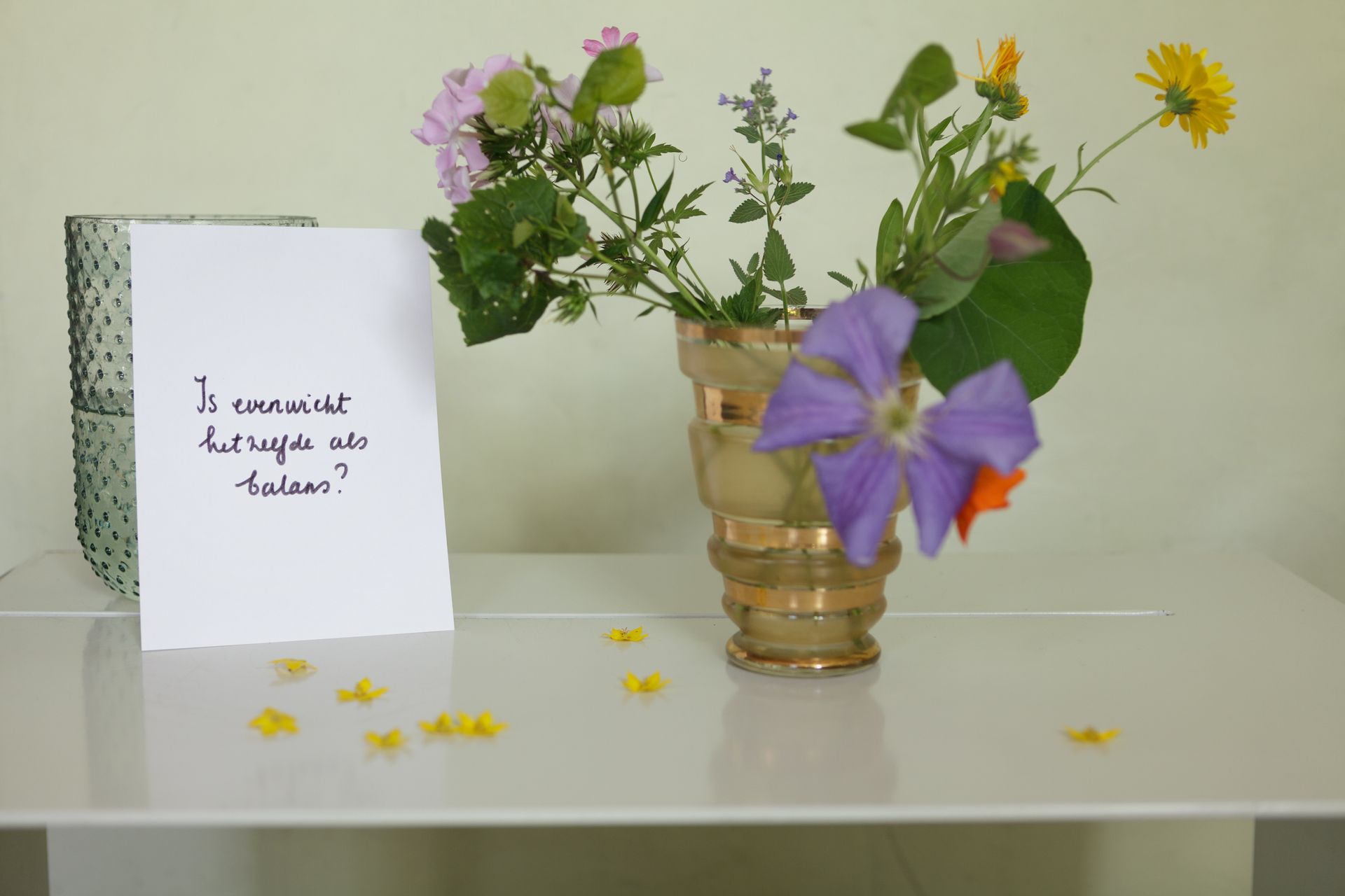 Bloemen in een vaas met een kaartje erop, , op een witte tafel.Foto Elise Klinkert