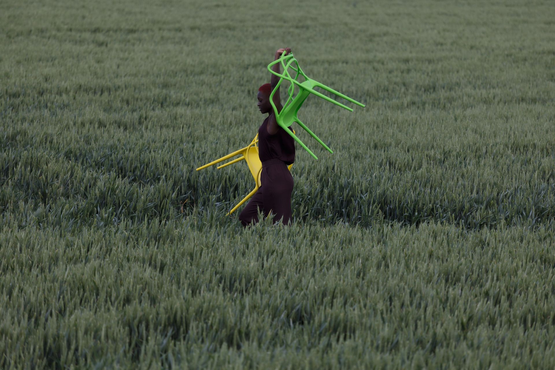Een persoon draagt ​​gele en groene stoelen in een veld met groen gras. Foto Elise Klinkert
