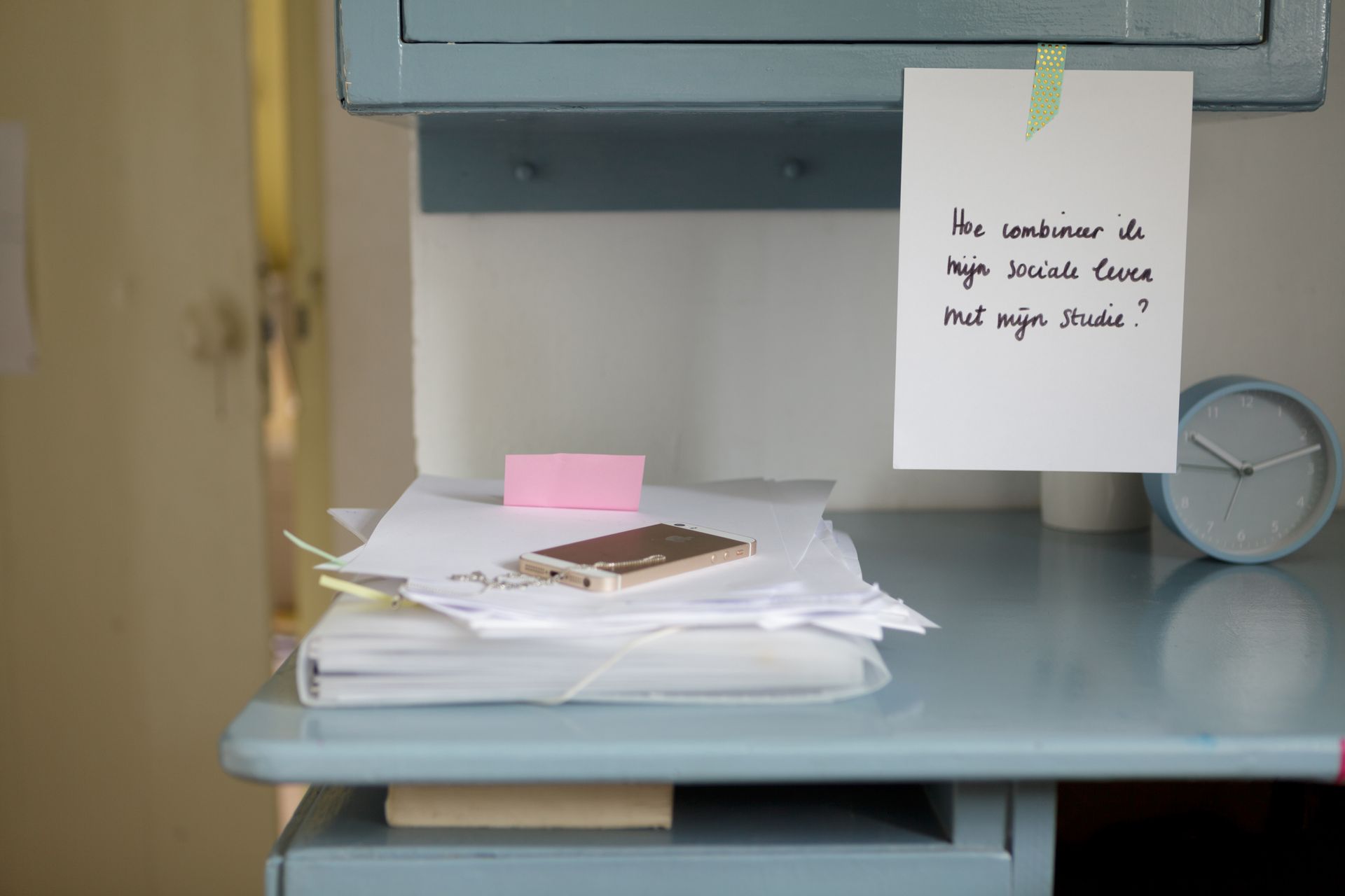 Bureau met papieren, een plakbriefje en een klok. Foto Elise Klinkert
