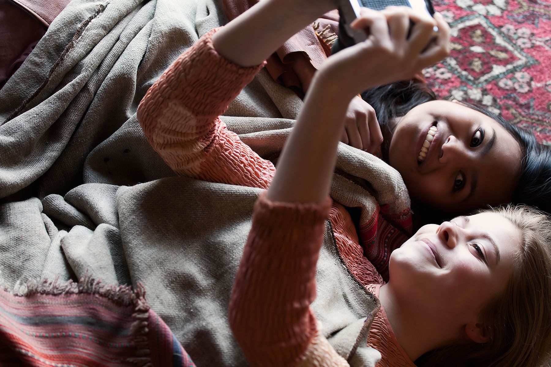 Twee jonge vrouwen liggen lachend onder  een deken  en maken een selfie.Foto Elise Klinkert