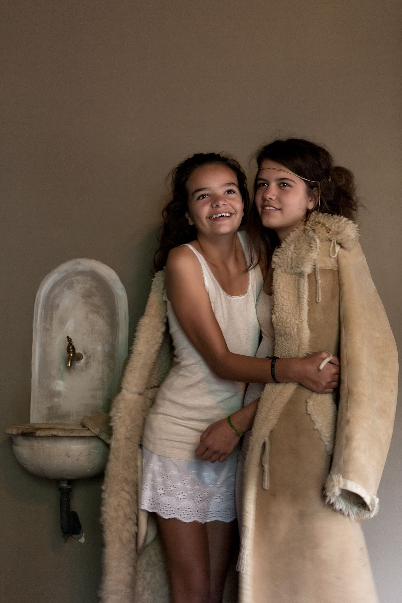 Twee meisjes omhelzen elkaar, de een in een jurk, de ander in een lange jas, bij een fonteintje.Foto Elise Klinkert
