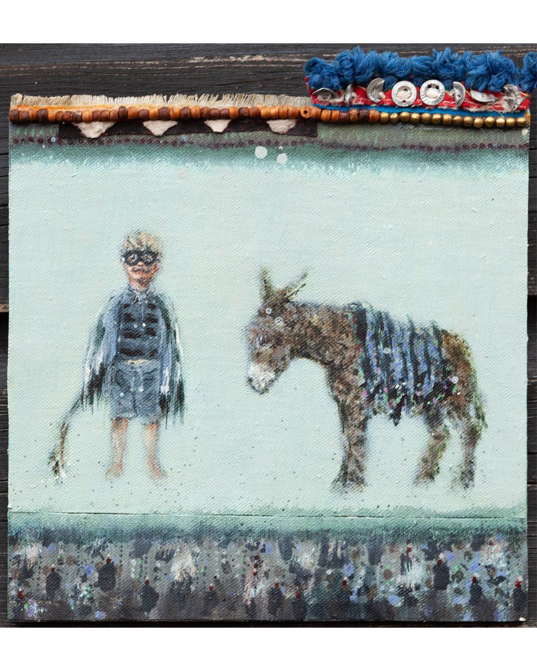 Kind met ezelje, staand voor een lichte achtergrond. Boven en onder versierd met blauwe, bruine en witte stof.