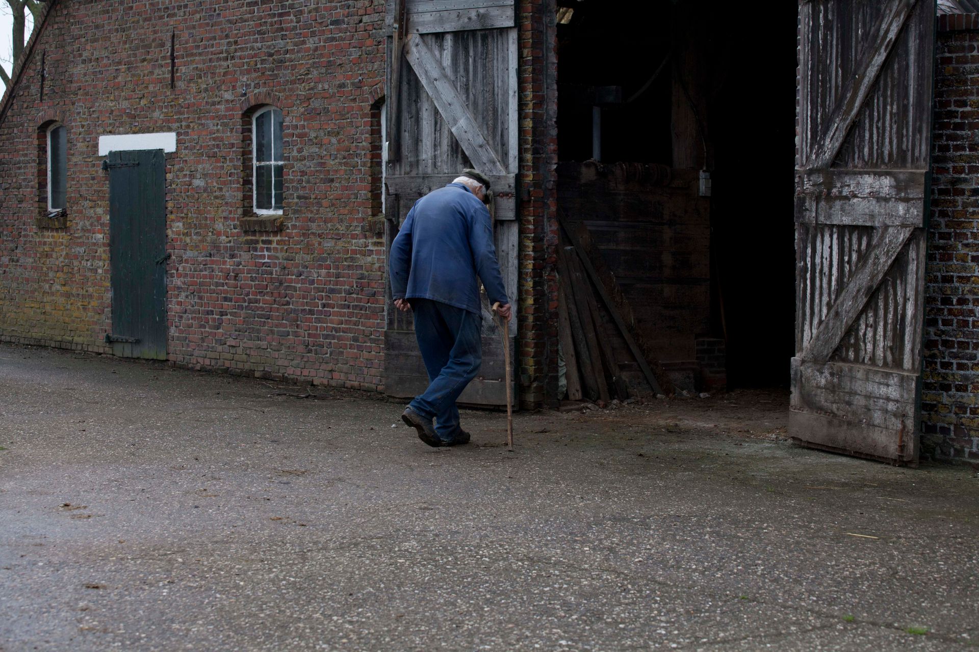 Een man in overall  loopt naar een grote, open schuurdeur van een bakstenen schuur.Foto Elise Klinkert