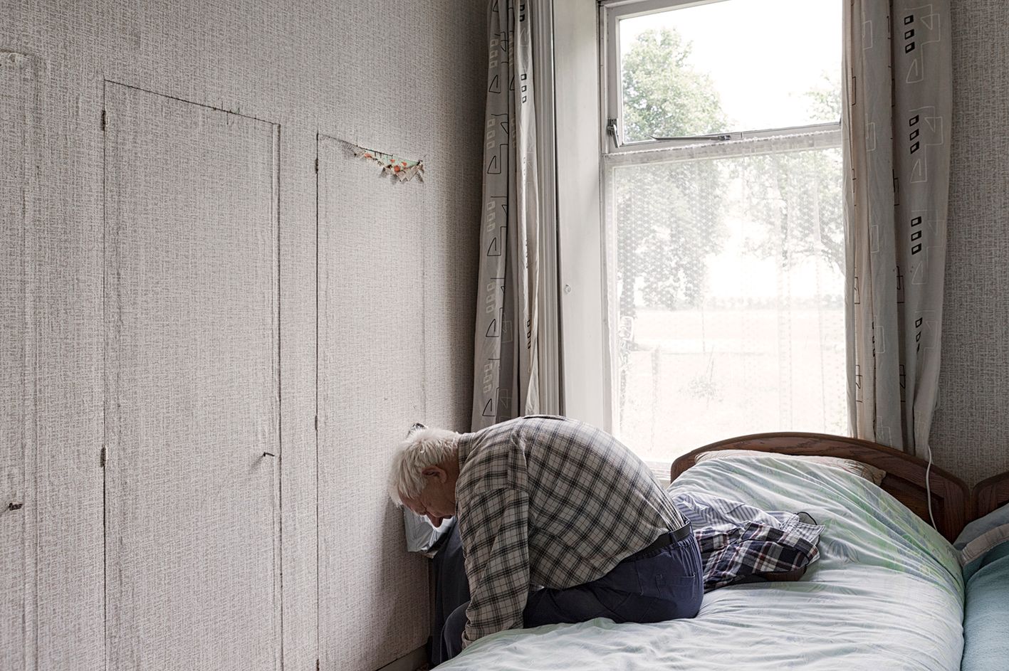 Een oudere man zit ineengedoken op bed. Foto Elise Klinkert