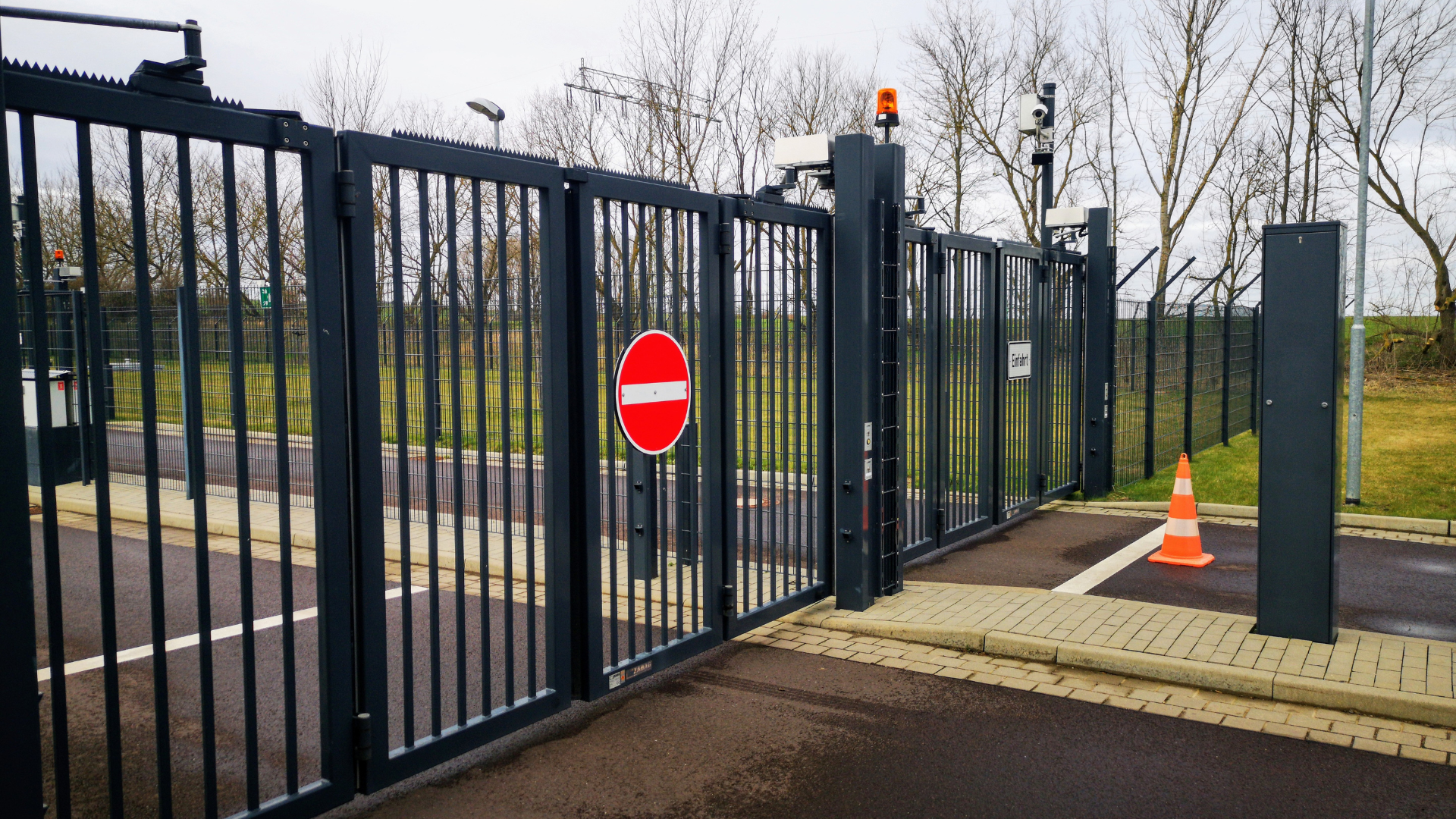 Black metal gate with a red no-entry sign and orange cones blocking a driveway entrance