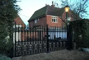 Brick house behind ornate black iron gate at dusk, with a lit streetlamp and bare trees.