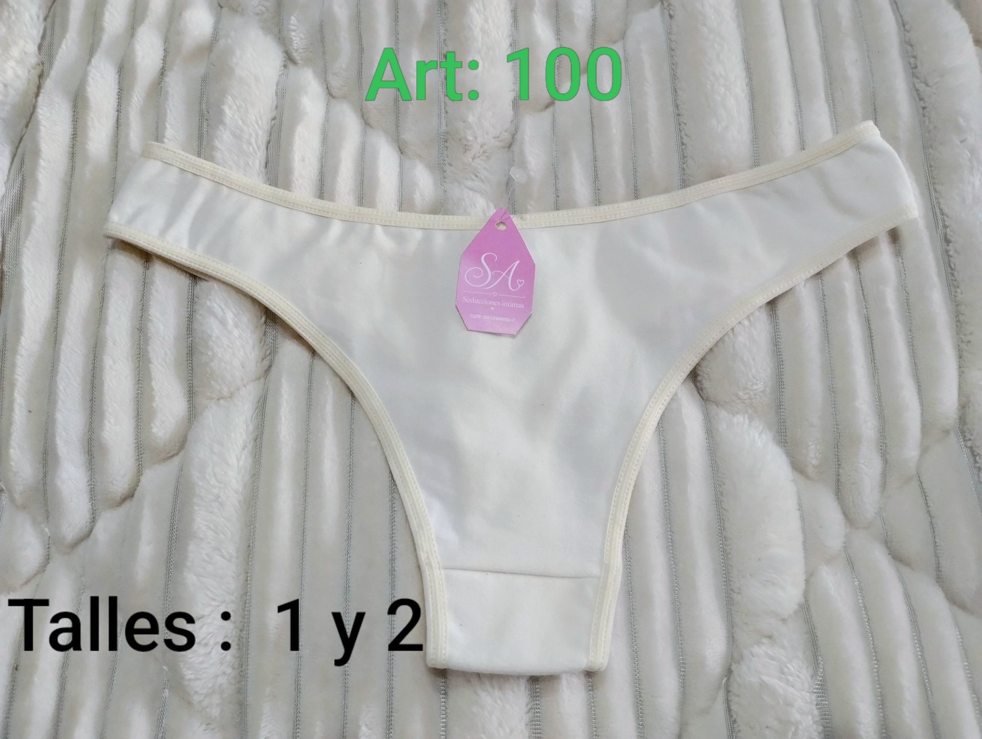 Tanga blanca con ribete de encaje sobre un fondo acanalado, con las etiquetas «Art 100» y «Talles 1 y 2»